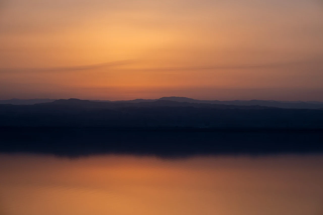 Amber dawn glowing above dark, still water