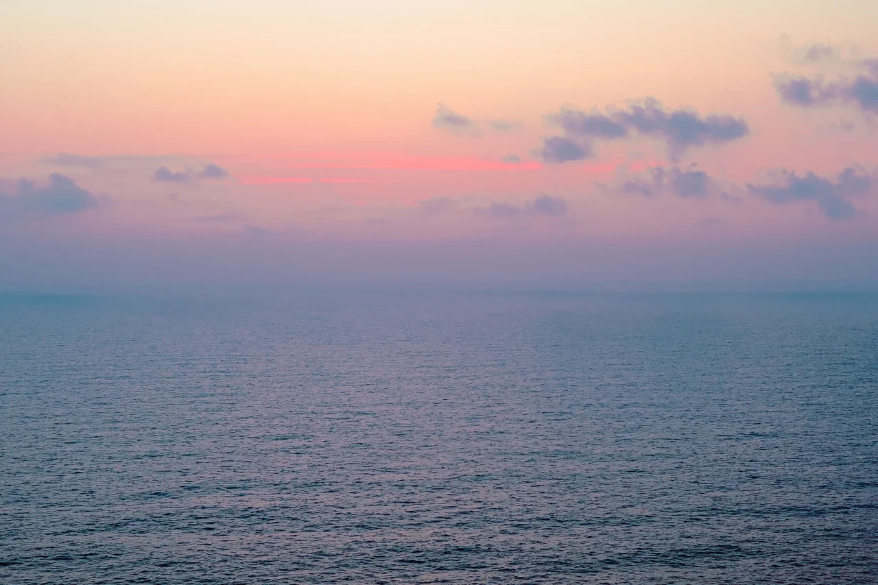 A calm sea at sunrise beneath a soft pastel sky
